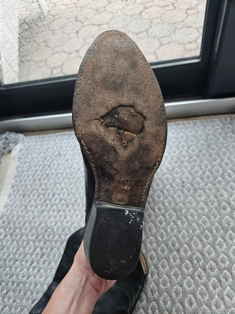 The worn leather sole of a cowboy boot, worn through near the toe, before the repair